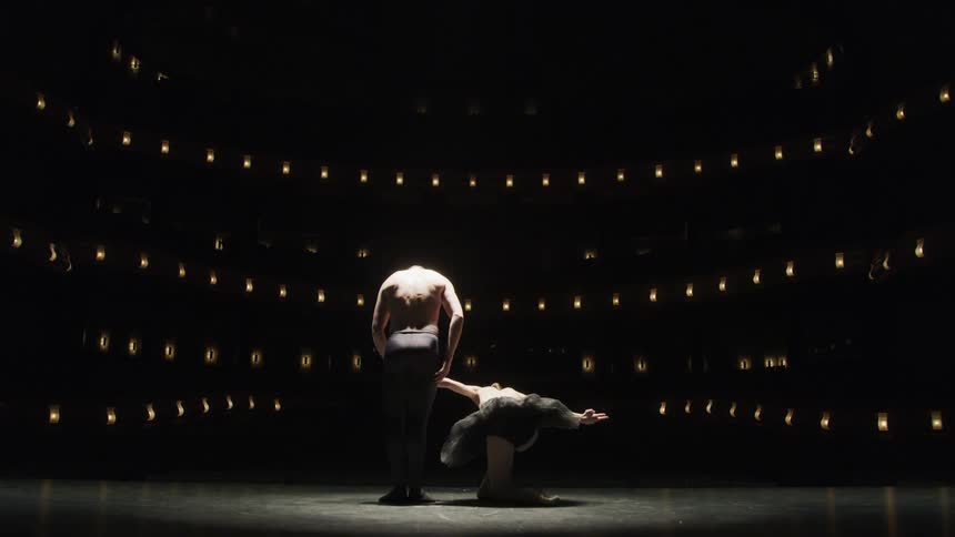 Two ballet dancers take a bow on the stage of a grand theatre facing an unseen audience