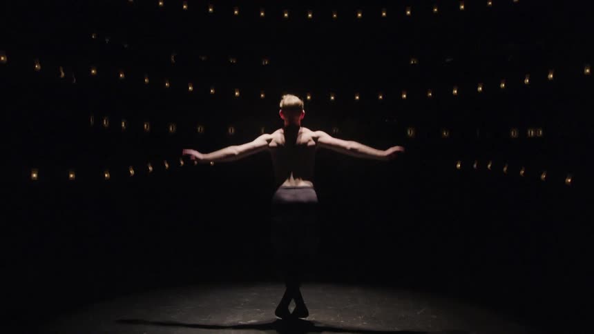 Male ballet dancer dressed in tights performs on stage in a dark theater