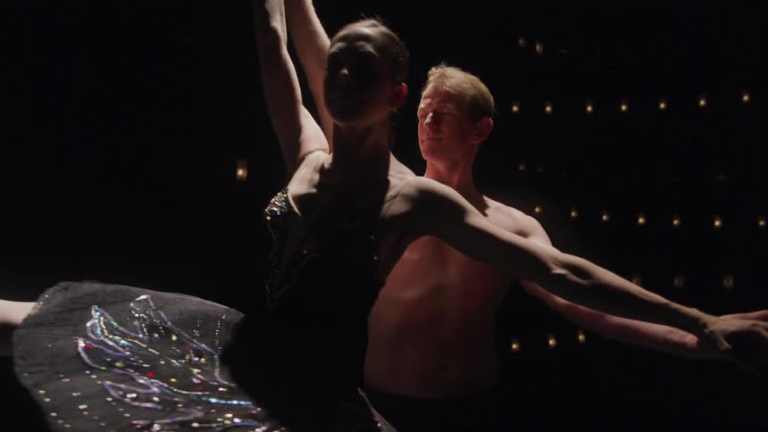 Two ballet dancers perform a lift on stage with one holding the other aloft in a poised graceful position
