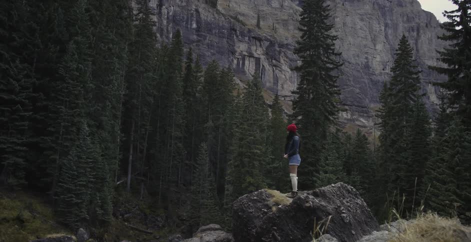A woman stands on a large boulder in a mountain forest