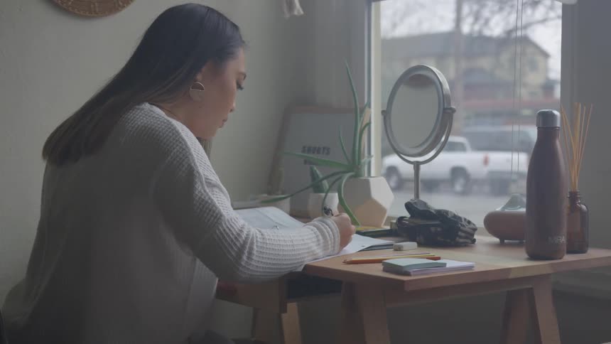 Woman sitting at a table reading a book and holding a pen