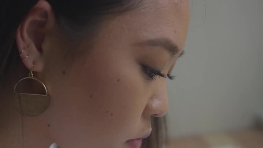A close up of the profile of a woman focused on a task wearing multiple piercing and a large gold earring