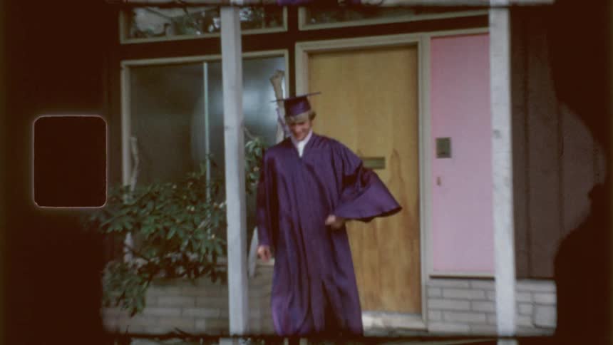 A graduate exits the home in his cap and gown