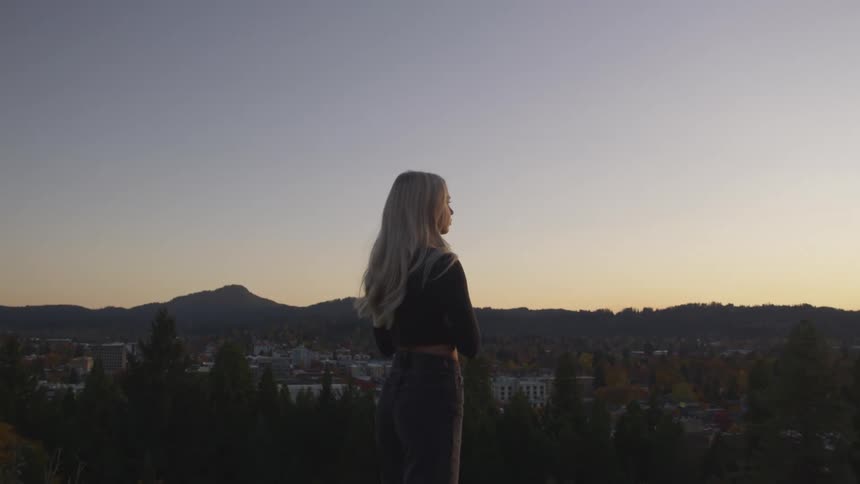 Woman in a natural environment in the late afternoon observing the landscape of a city and mountains in the background