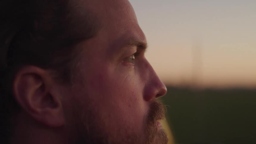 Side portrait of a bearded man outdoors enjoying the view of a field at dusk