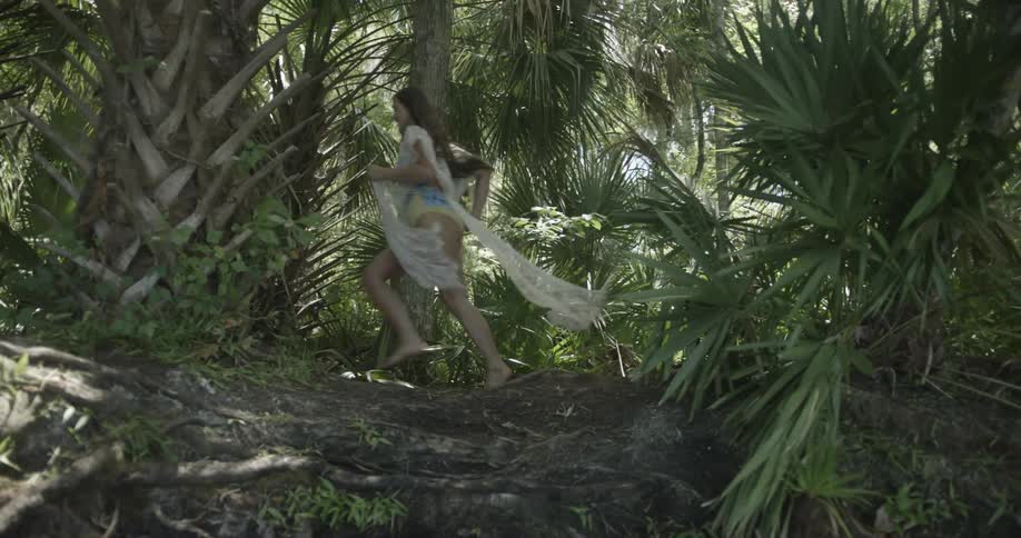 A woman sprints through palm trees in a tropical area