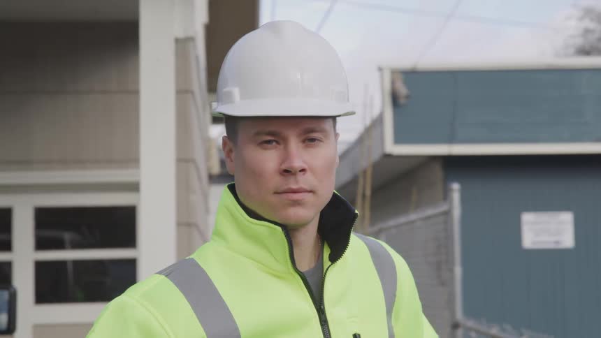 Male worker wearing protective gear stands under the power lines passing between buildings during the daytime