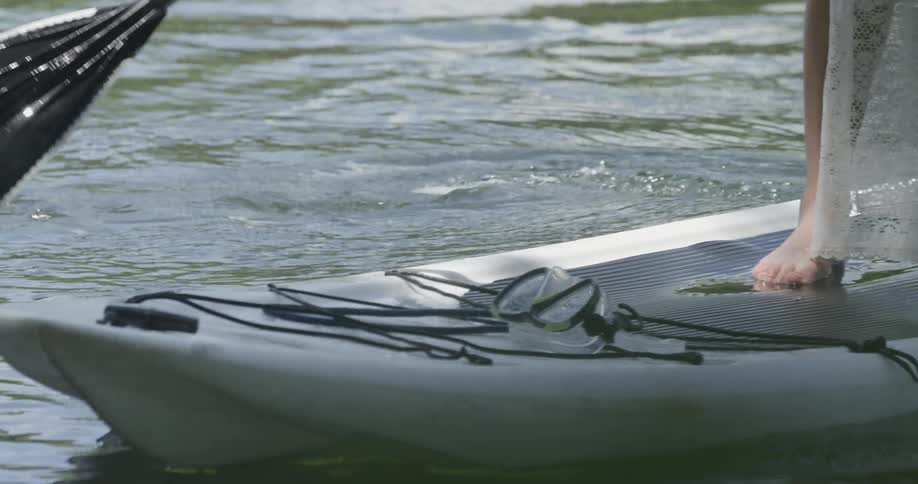 A woman stands on a paddle board and paddles on a body of water