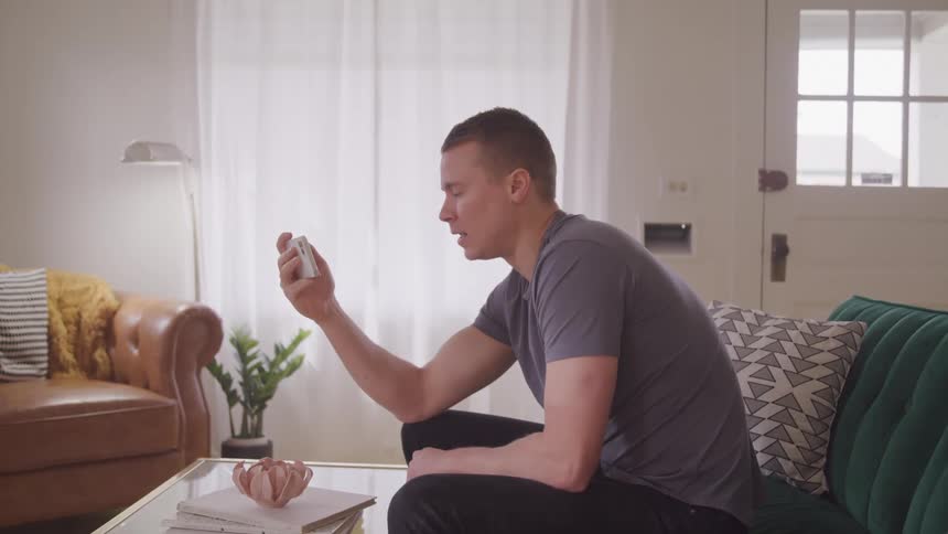 A young man sitting on the couch while chatting with someone on his smart phone