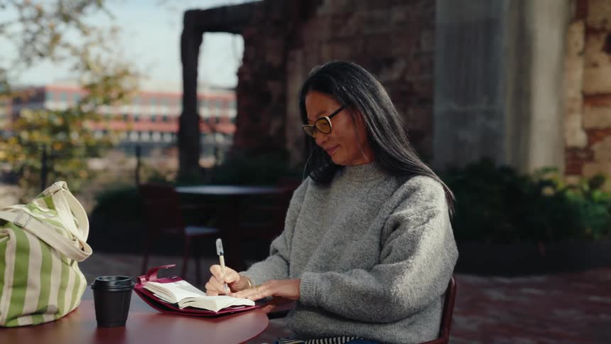 Woman sitting at a table outdoors writing in a notebook