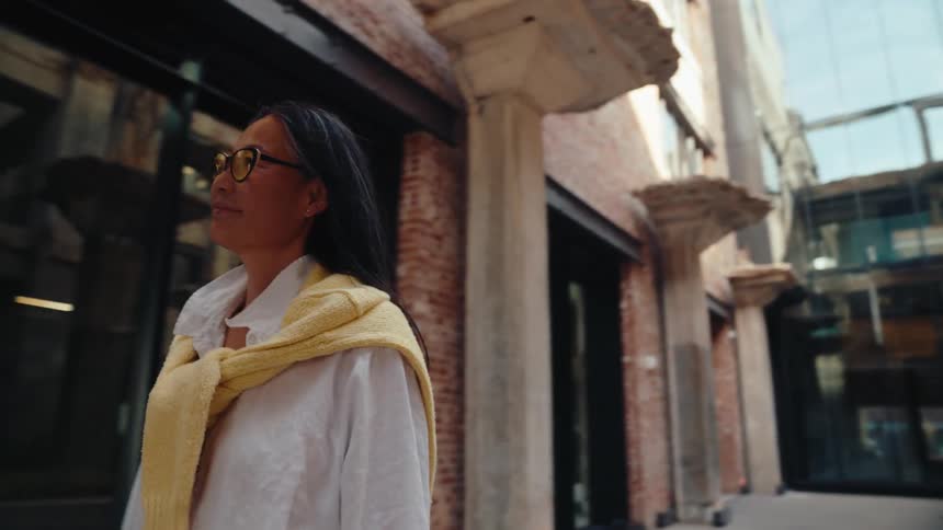 Woman wearing glasses and with a happy facial expression walking outdoors in an environment surrounded by rustic buildings