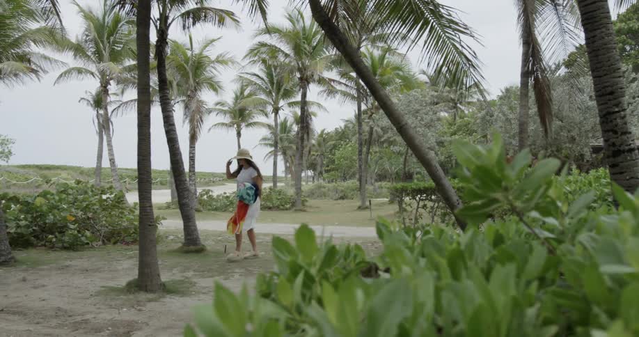 A woman walks near palm trees in a tropical area