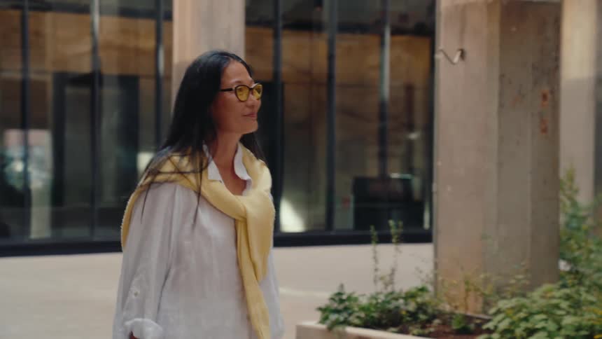 A woman smiles as she strolls through a downtown area outside buildings