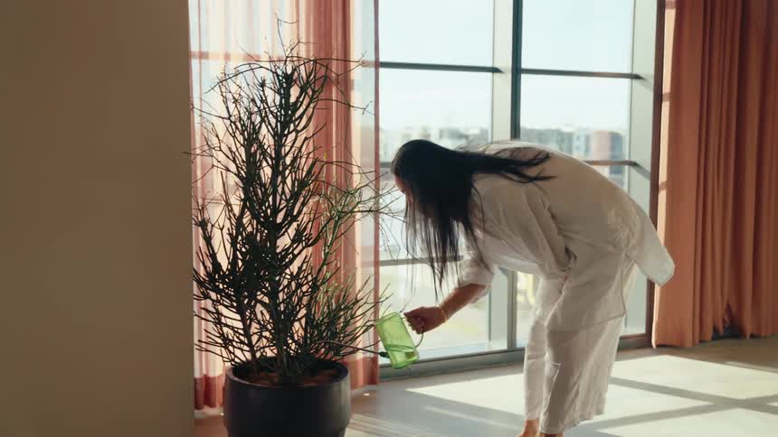Woman arranging chairs at a table and pouring water into a potted plant