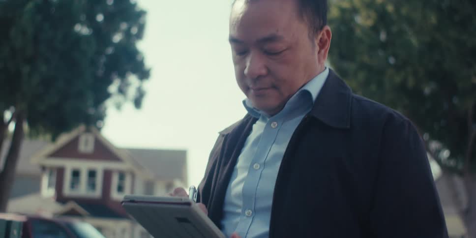 A person sits on a bench in a residential neighborhood writing on a tablet with a stylus