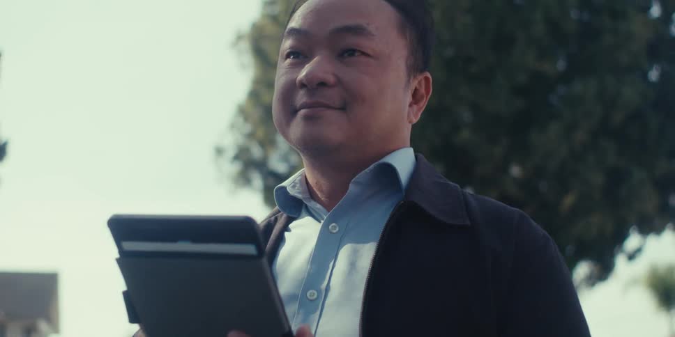 Man standing outdoors with happy facial expression interacts with a tablet