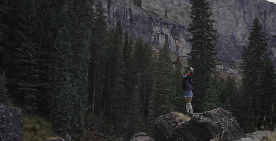 A woman standing on a boulder and lifting her arms to the sky