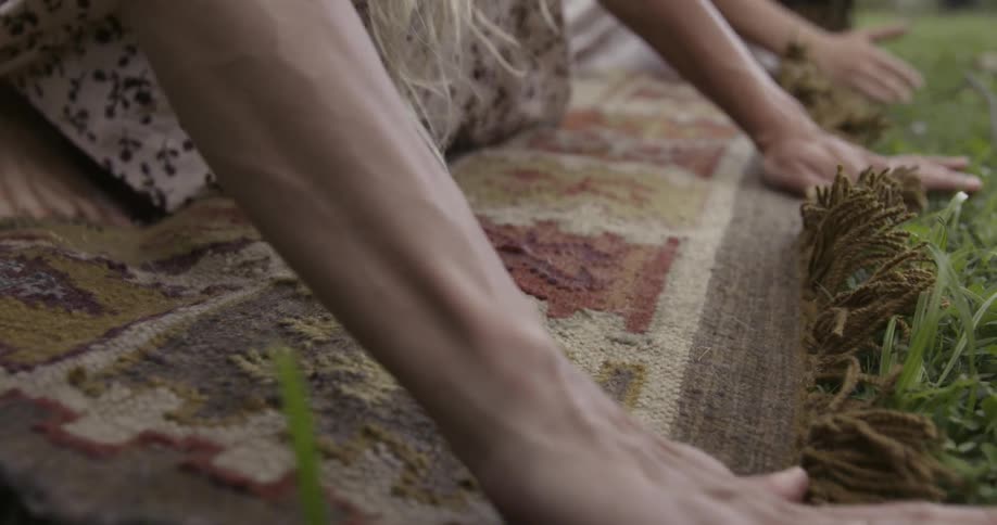 A woman rolls out a rug on a grassy lawn