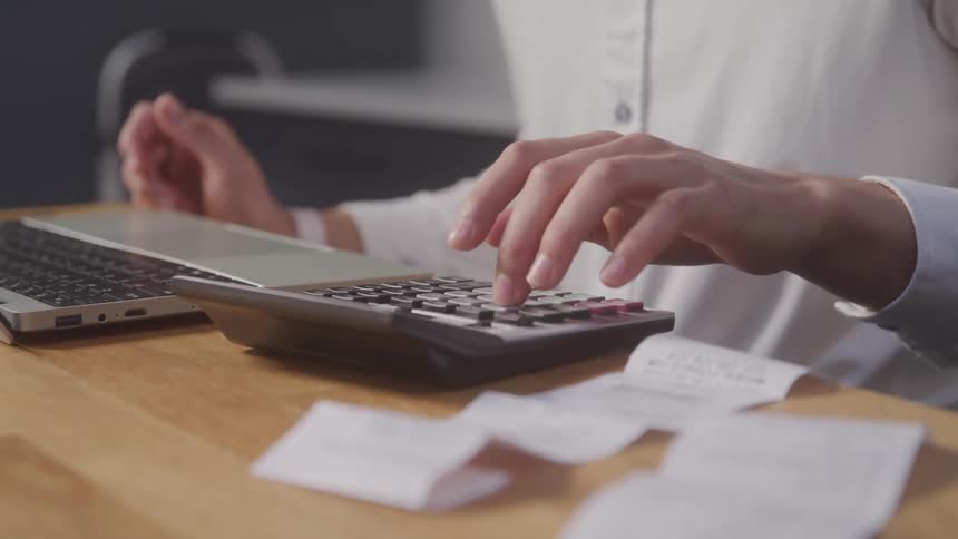 A woman is sitting at a desk with a laptop and using a calculator