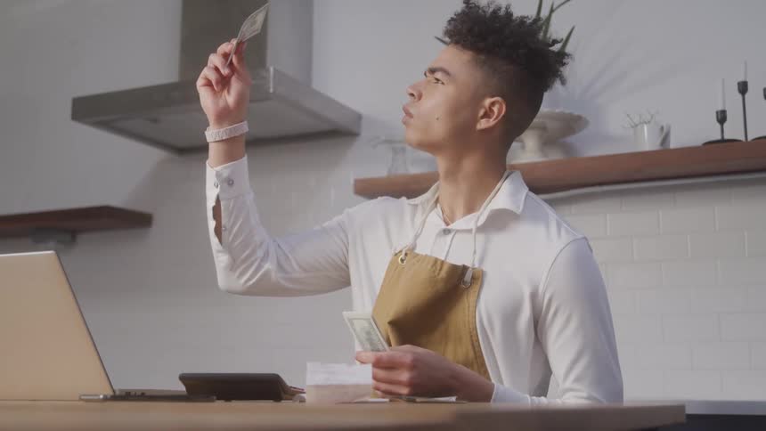 Man in an apron is holding a banknote