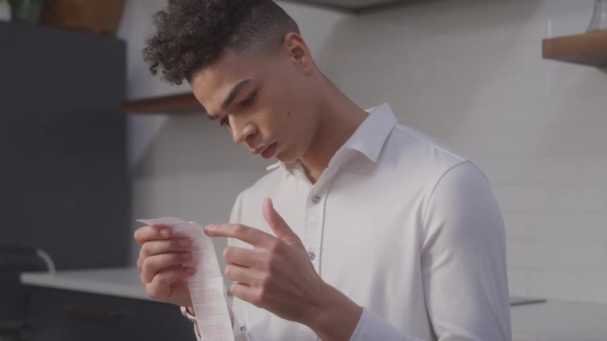 Young man standing carefully analyzing a receipt
