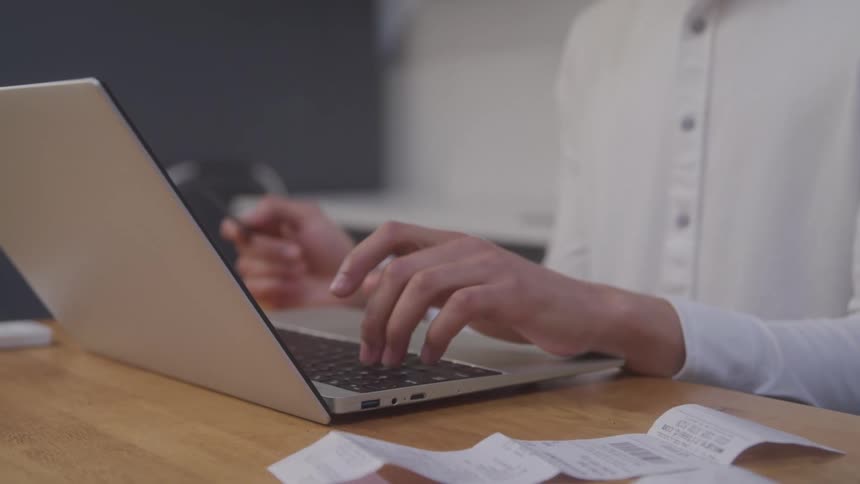 Pair of hands of a person interacting with an open laptop on a table