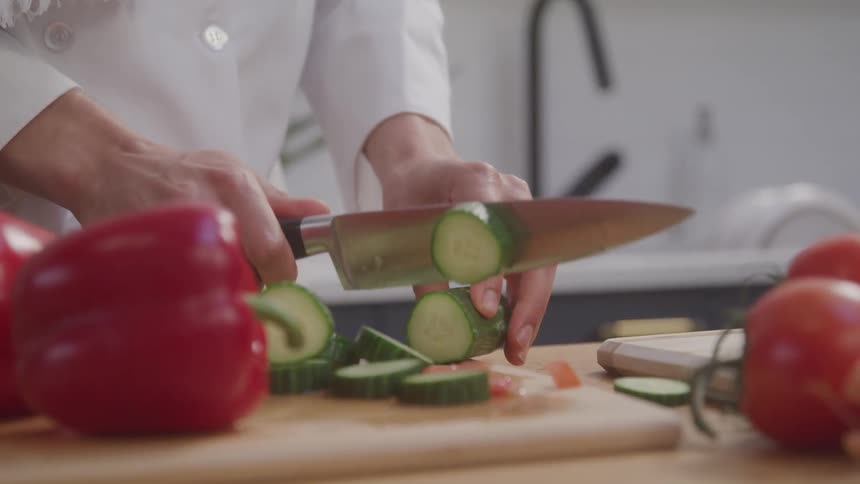A chef is cutting a cucumber on a cutting board in a kitchen