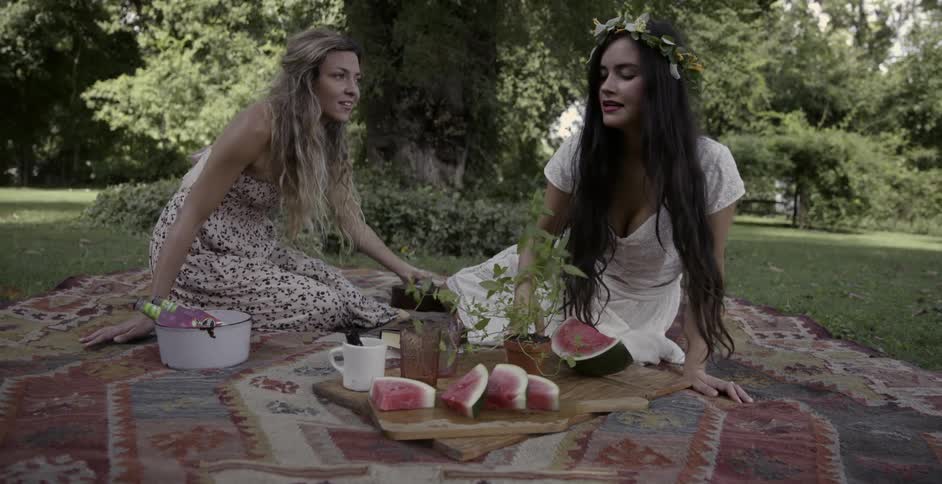 Two women sitting down on picnic blanket to eat watermelon