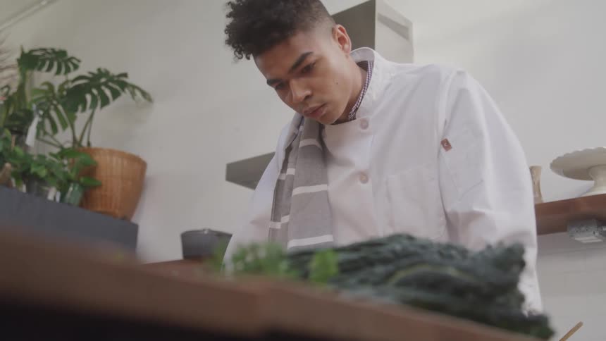 Young man in a white apron looking down at a table with vegetables