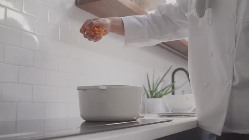 A chef drops vegetables into a pot on a stovetop in a kitchen