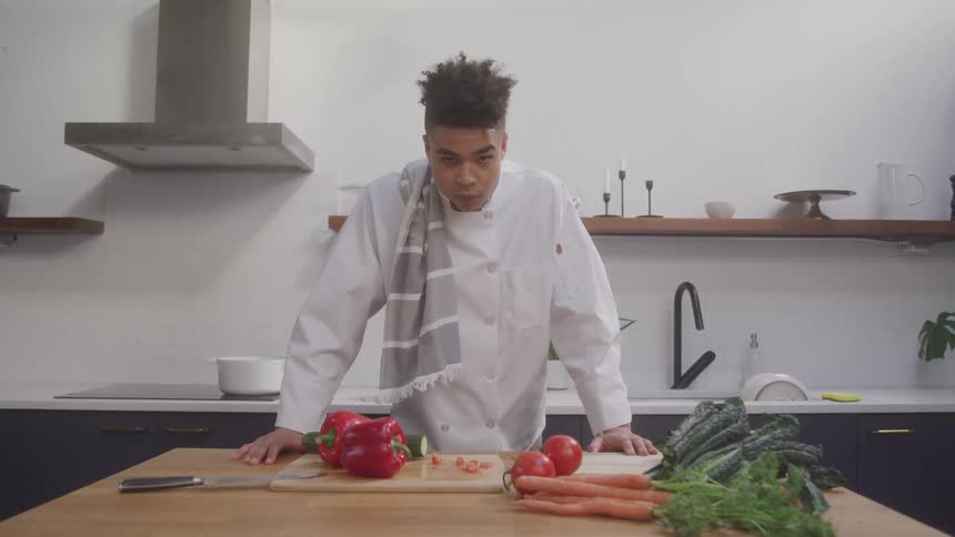 Chef in a white apron with cut vegetables on the table