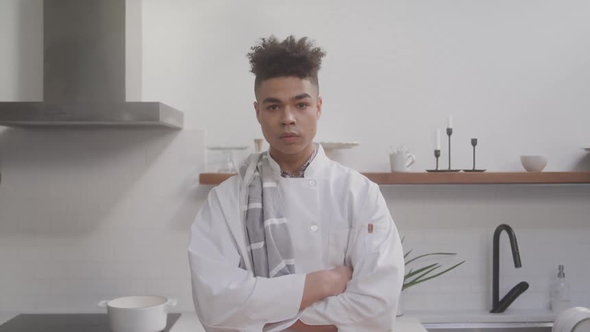 A chef tilts his head up and smiles in the kitchen