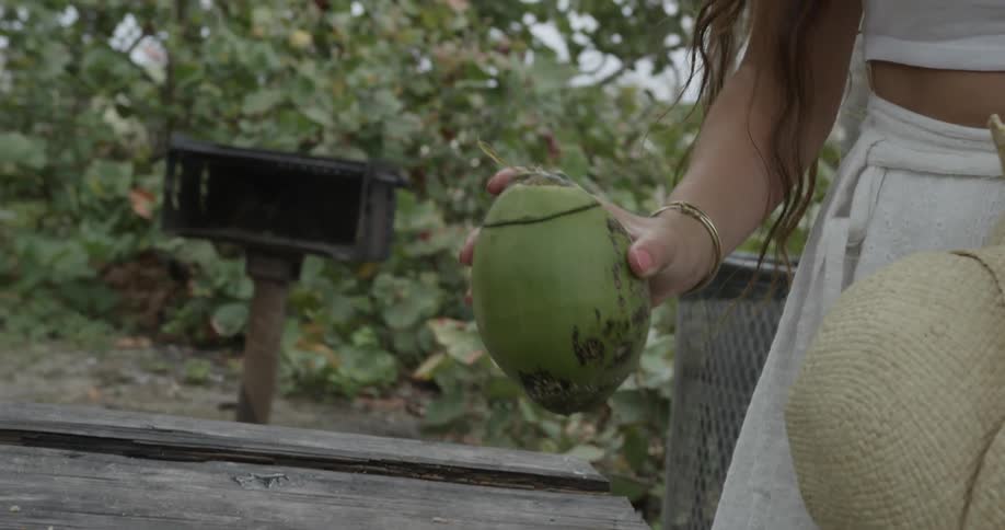 A woman picks up a green coconut from a picnic table