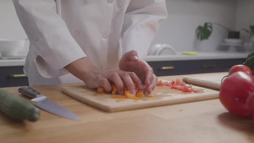 A male chef picks up chopped yellow tomatoes from a wooden cutting board