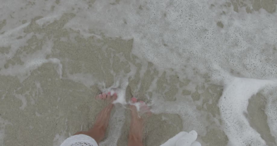 A wave rolls over a woman's bare feet at the beach