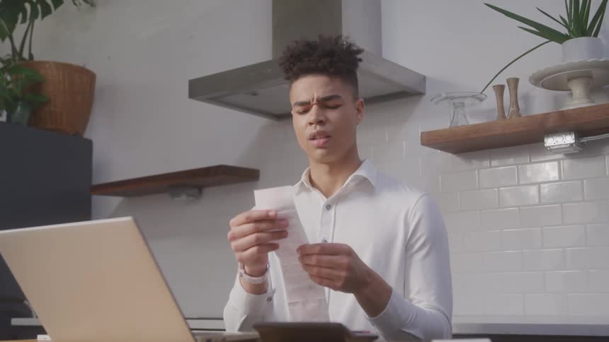 Man sitting down grimacing as he sees a receipt