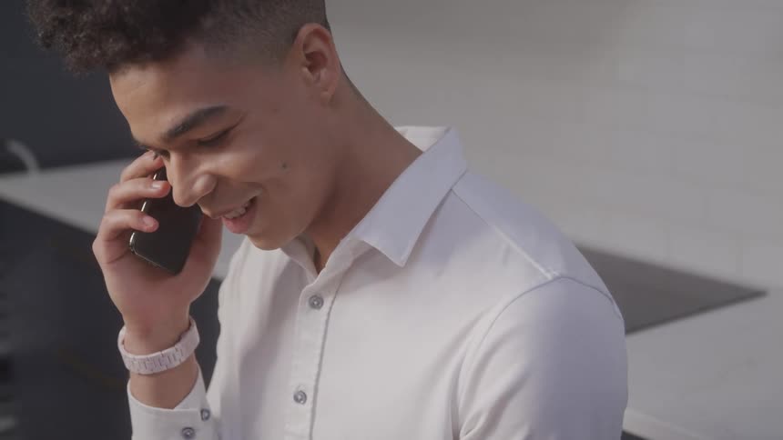 A young man with curly dark hair and a white collared shirt in a phone conversation