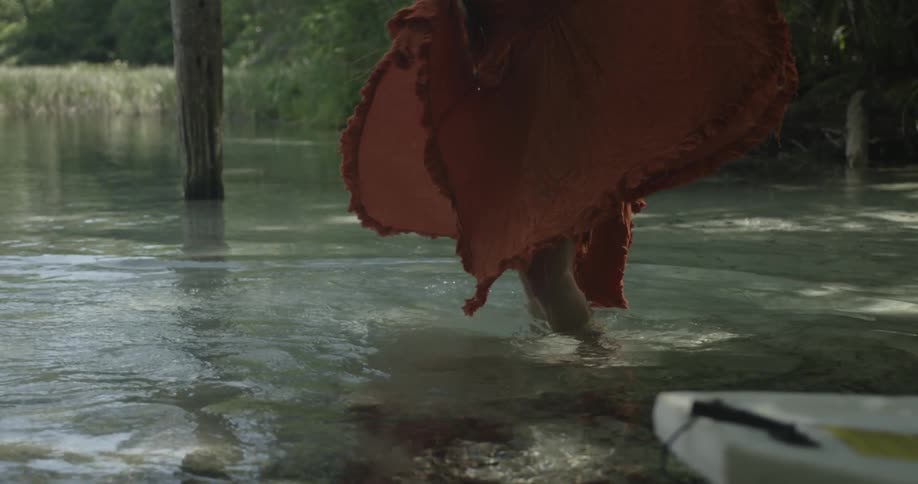 Woman in red dress wading in a shallow pond