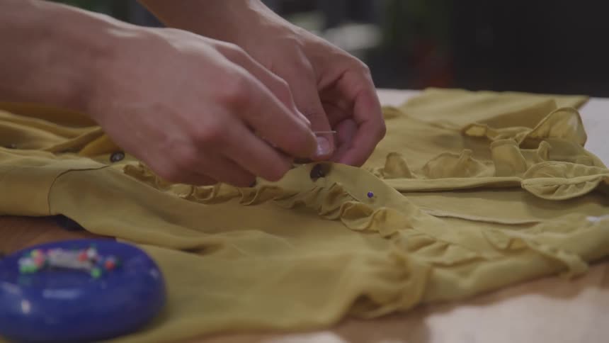 Pair of siblings delicately placing buttons on a beige jumpsuit