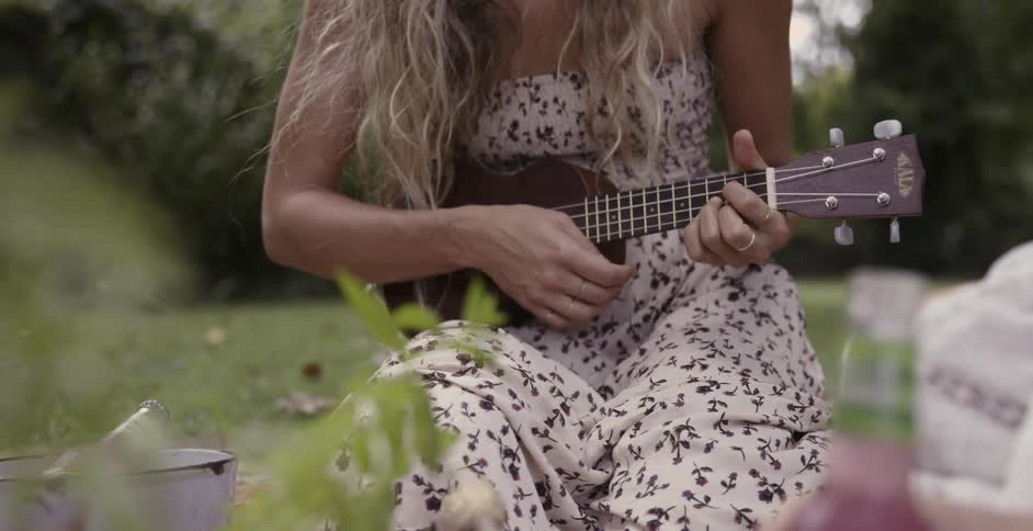 A woman is sitting in a park playing a ukulele