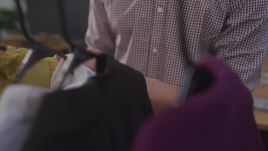 Pair of hands of a person looking at shirts on hangers