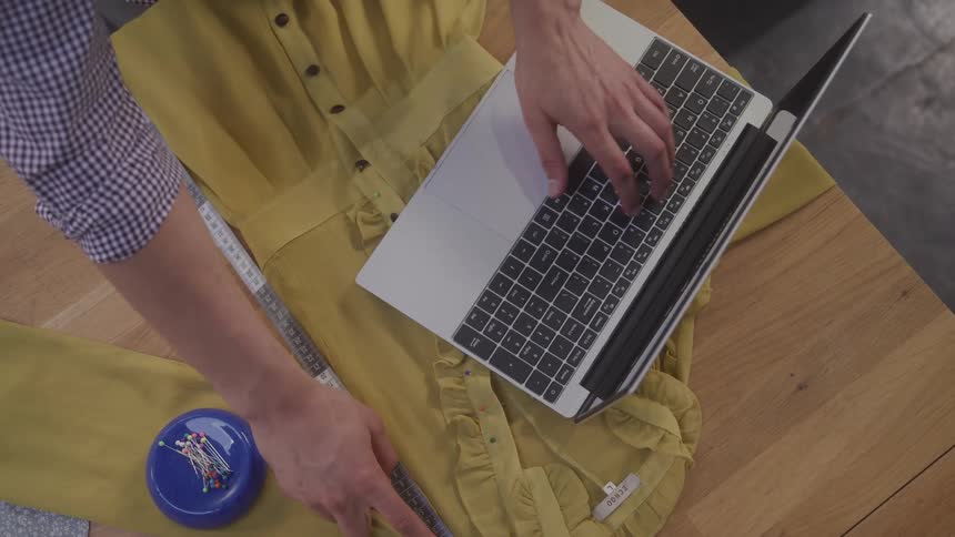 A tailor is using a laptop and measuring a dress