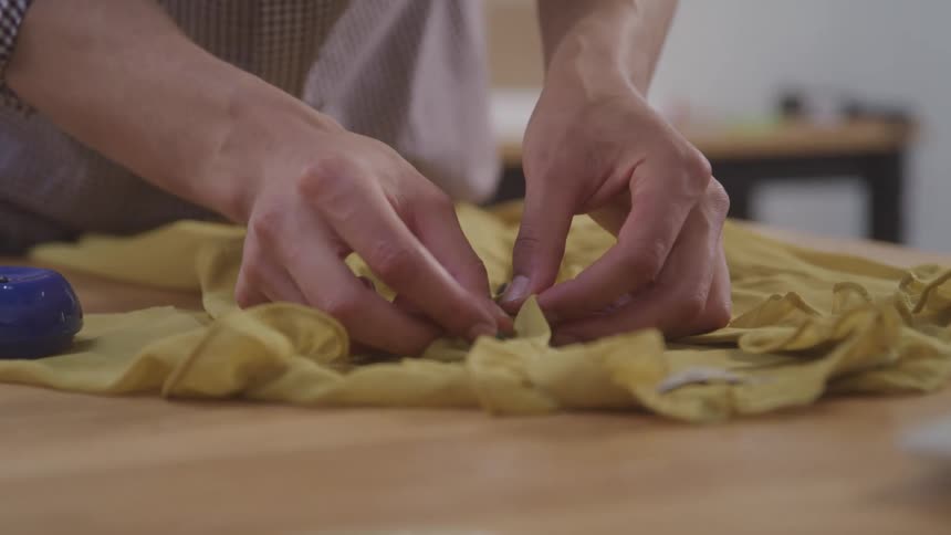 Close up of a pair of female hands working on a yellow blouse on the table