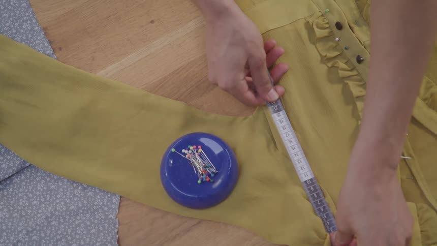 A woman uses a measuring tape on a dress on a table