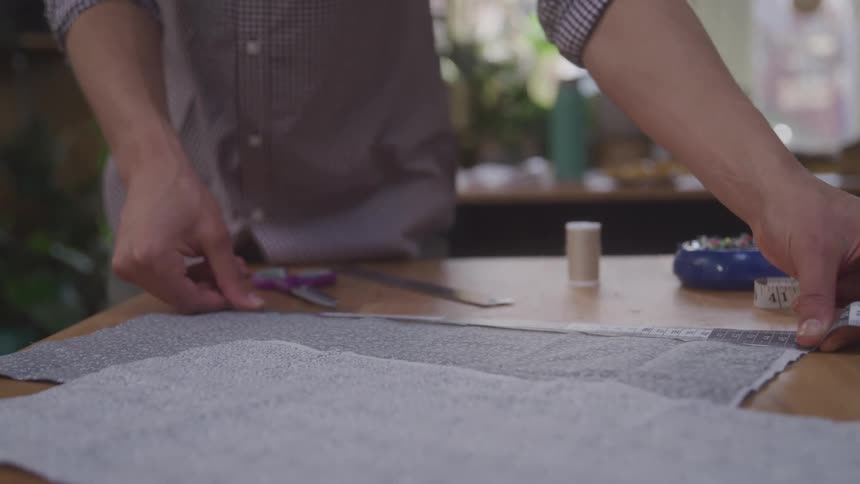 A person measures a piece of fabric on a wooden table with a ruler and measuring tape