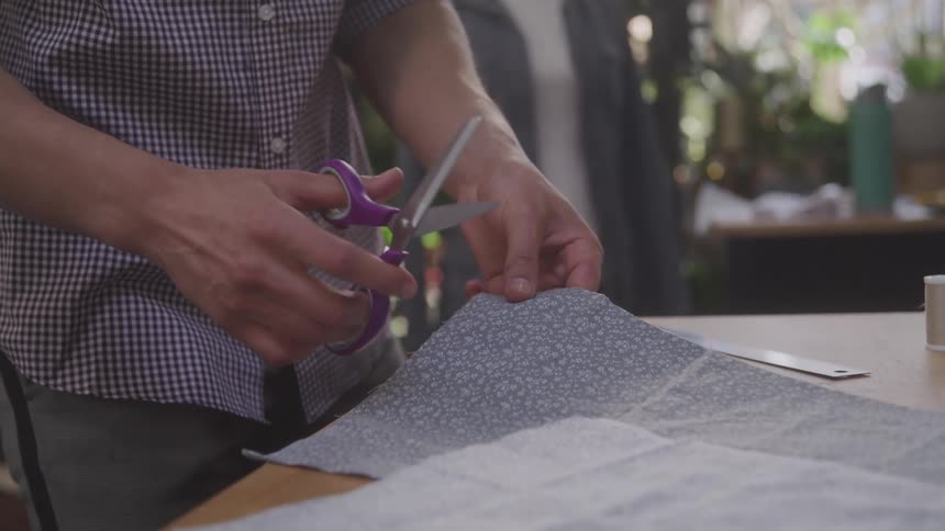 Pair of hands with scissors working with fabric on top of a table