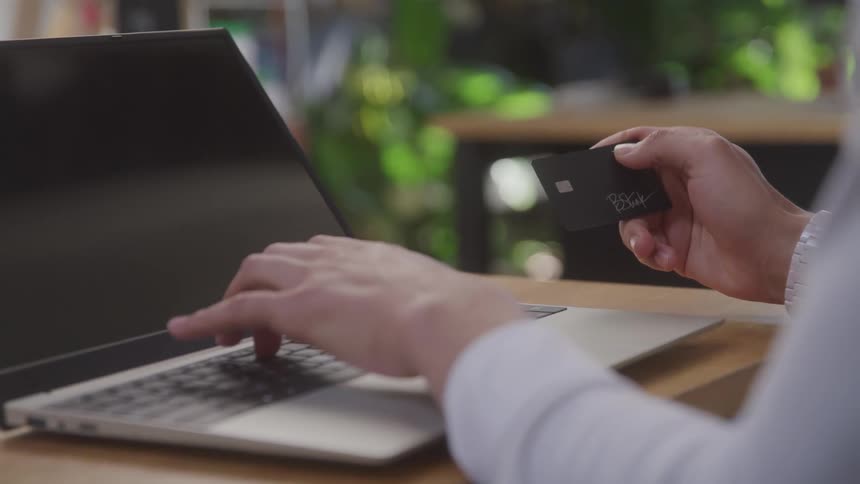 Hand holding a black card and the other hand typing on a laptop