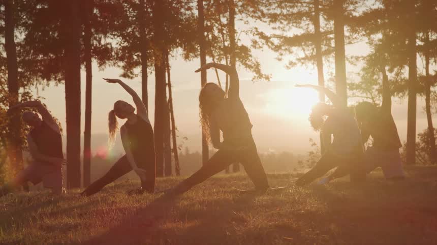 Five people practicing yoga outdoors at dawn and all in sync