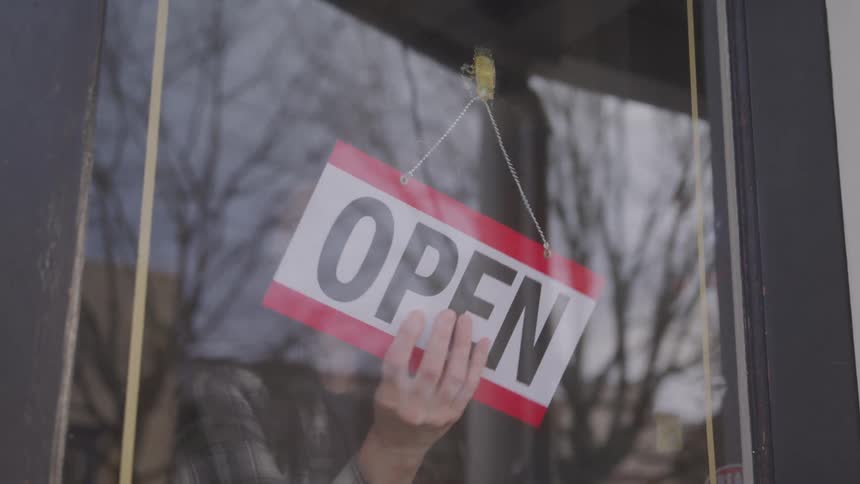 Woman turning the closed sign to open on a glass door of a store