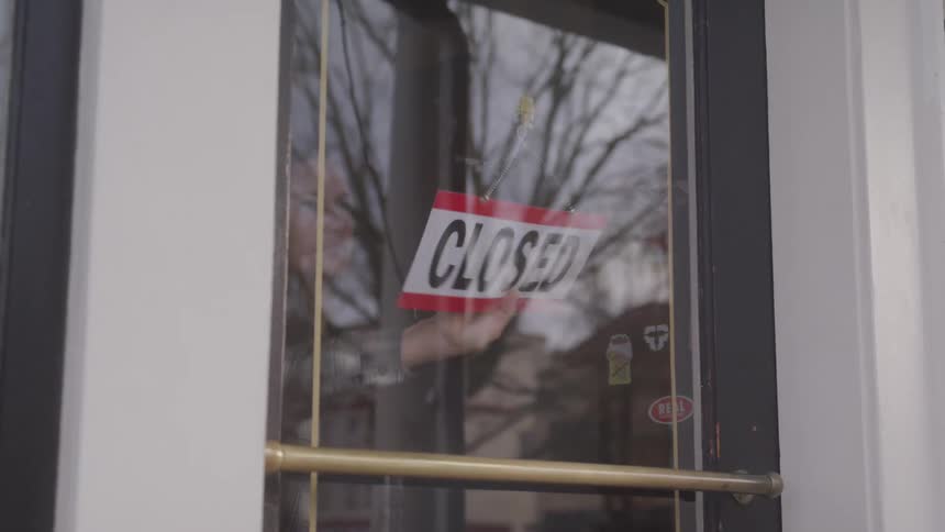 A man turns the sign to open on the shop door